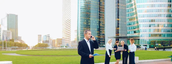 Businessperson talking by smartphone with employees in backgroun