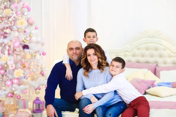 Jóvenes padres felices sentados con hijos cerca de abeto en la cama . — Foto de Stock