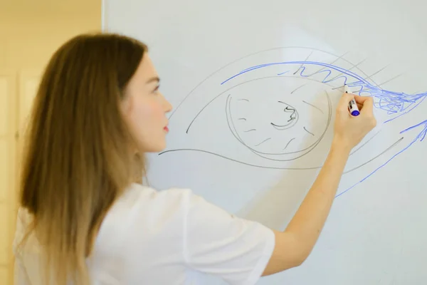 Jeune cosmétologue attire l'attention sur la plaque au cabinet de cosmétologie, se concentrer sur le dessin . — Photo