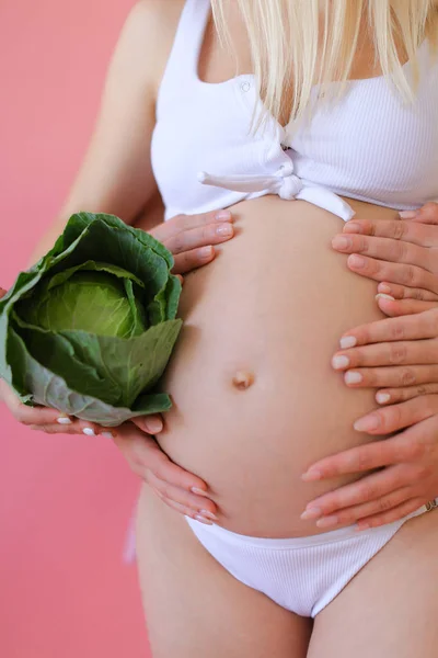 Крупным планом беременная женщина в нижнем белье держит живот и держит капусту . — стоковое фото