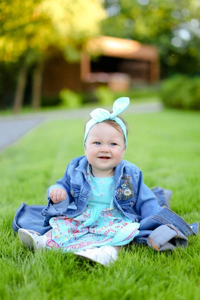 小微笑的女孩坐在绿草上, 穿着牛仔裤夹克. — 图库照片