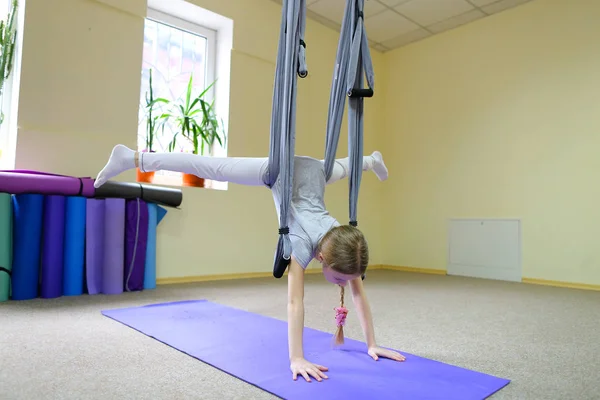 Schoolgirl sits on twine on acrobatic ropes.