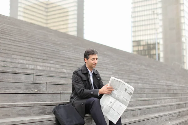 male business tutor sitting on stairs and reading newspaper