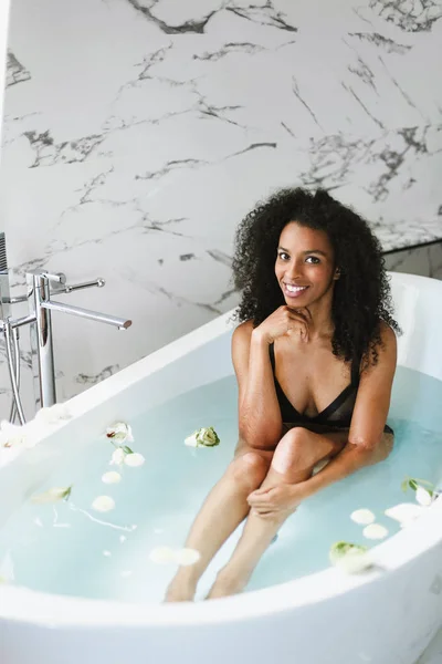 Young afro american girl sitting in bath, wearing black swimsuit. — Stock Photo, Image