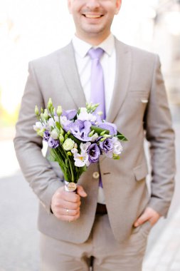 Buket çiçek tutmak ve gri takım elbise giymiş genç beyaz damat.