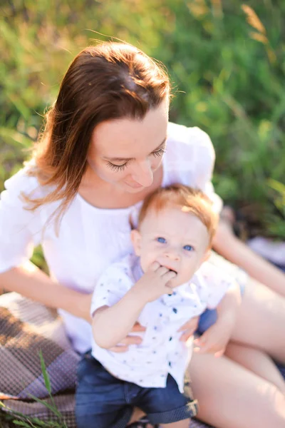 Giovane madre tenera baciare bambino piccolo su plaid, erba su sfondo . — Foto Stock