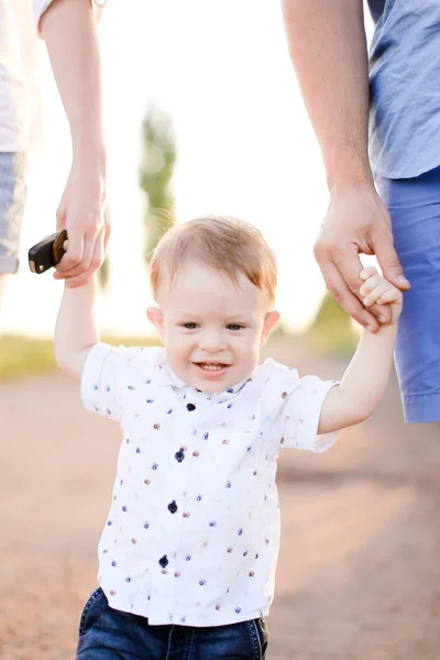 Piccolo bambino sorridente che tiene per mano i genitori e cammina sulla strada . — Foto Stock