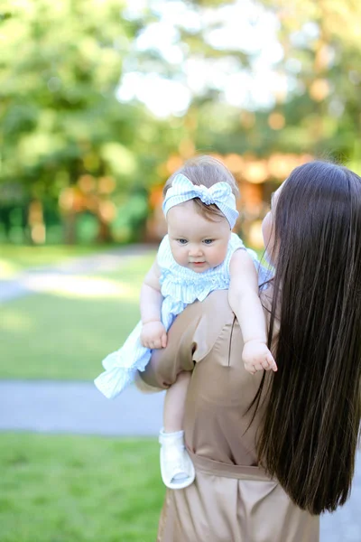 Widok z tyłu z młoda brunetka kobieta trzyma małego dziecka w ogrodzie. — Zdjęcie stockowe