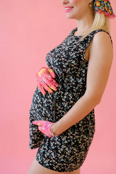 Jovem grávida segurando barriga e usando luvas em fundo monofônico rosa . — Fotografia de Stock