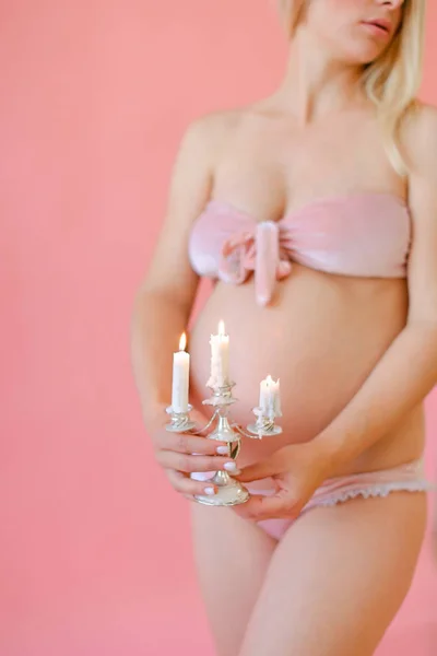 Loira feliz mulher grávida em roupa interior segurando barriga e mantendo velas . — Fotografia de Stock