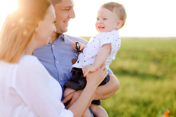Młodzi rodzice, trzymając dziecko, trawa w tle. — Zdjęcie stockowe
