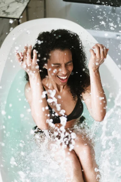 Young happy brown skin girl sitting in bath, wearing black swimsuit. — Stock Photo, Image