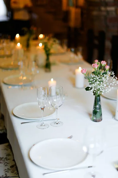 Bouguet bunga, piring putih dan garpu, lilin di atas meja . — Stok Foto