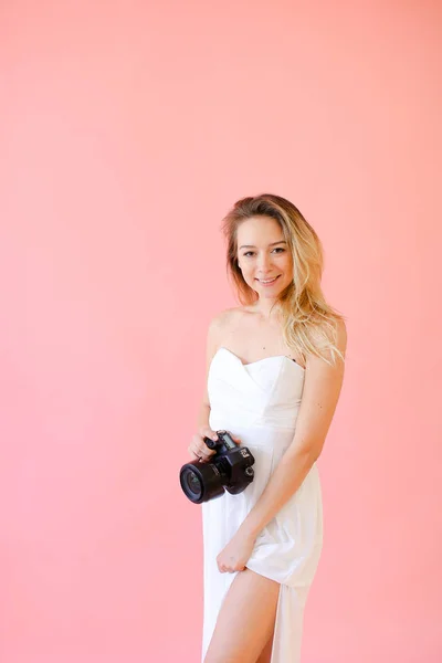 Jovem fotógrafa loira com câmera em fundo monofônico rosa . — Fotografia de Stock