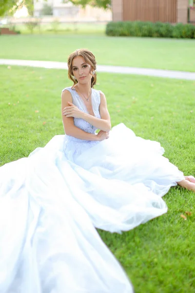 Καυκάσιος γοητευτική νύφη που κάθεται στο γρασίδι στο πάρκο, φορώντας λευκό φόρεμα. — Φωτογραφία Αρχείου