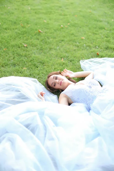 Невинная милая невеста, лежащая на траве в парке и в белом платье . — стоковое фото