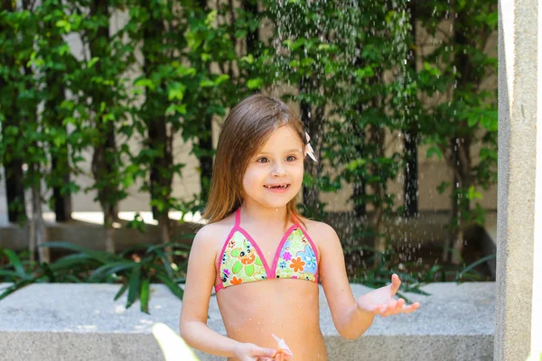 Gotas de agua caen sobre la niña en la ducha del traje de baño en d soleado — Foto de Stock