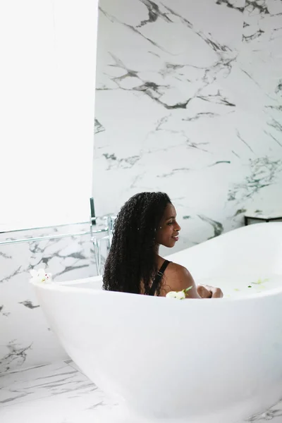 Afro american girl taking bath and relaxing in bathroom with marble tile. — Stock Photo, Image