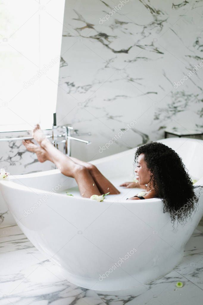 Young brown skin girl lying in bathroom with marble tile and relaxing.