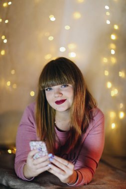 Pırıltı ekose üzerinde yalan ve smartphone, kullanarak genç kız arka planda çelenk.