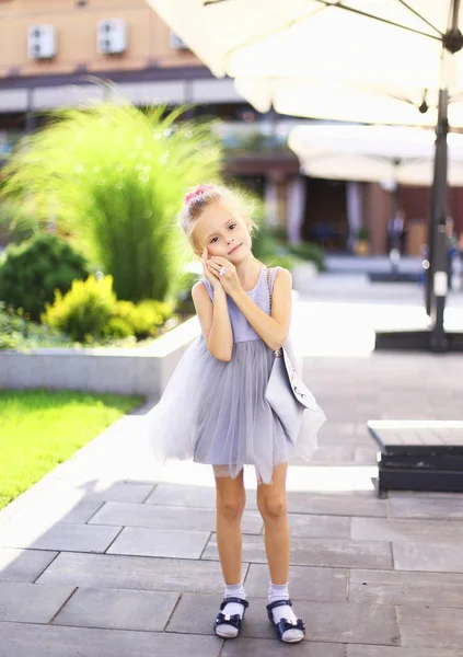 Bahçede duran ve gri elbise giyen küçük beyaz güzel kız. — Stok fotoğraf