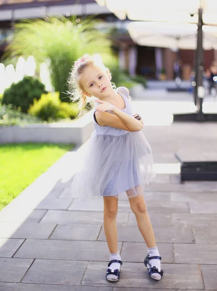 Pequeña chica bonita europea de pie en el patio y con vestido gris . — Foto de Stock