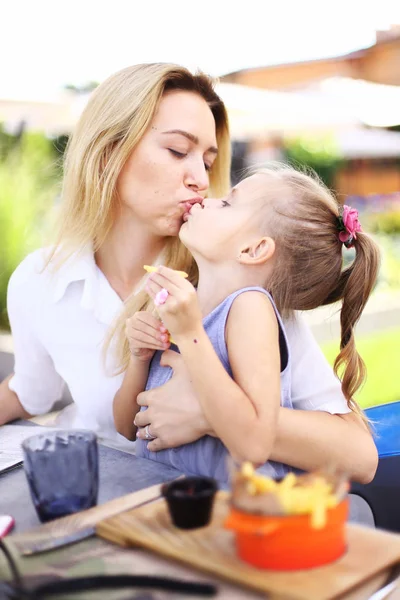 Young mother kissing little daughter eating French fries at street cafe. — Stock Photo, Image