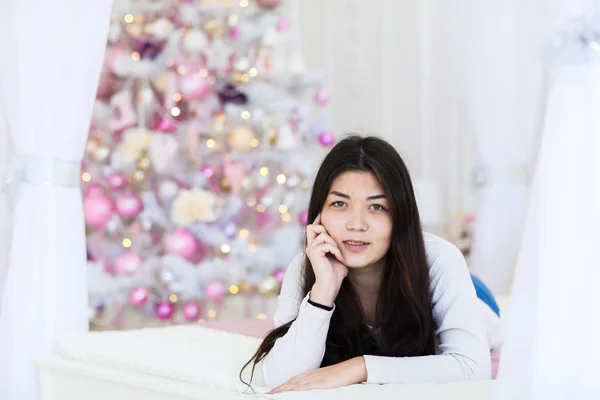 背景のぼやけた装飾されたモミの木でベッドに横たわって若い白人美少女. — ストック写真