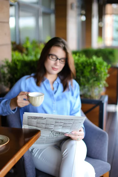 Mujer joven leyendo el periódico y utilizando el teléfono inteligente en el restaurante — Foto de Stock