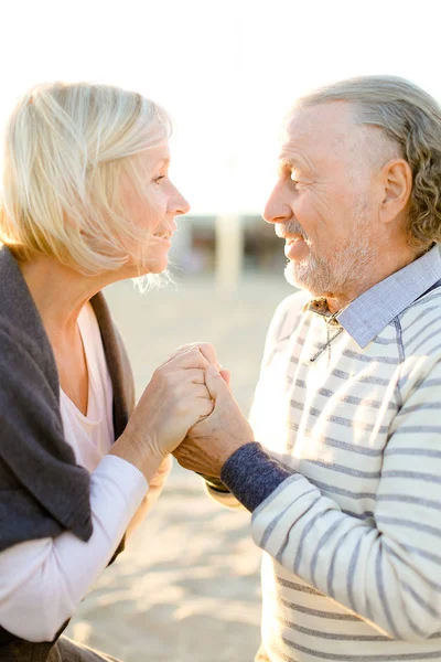 Yaşlı sarışın karısı tutan el kıdemli kocası ve kum plajda oturuyor.