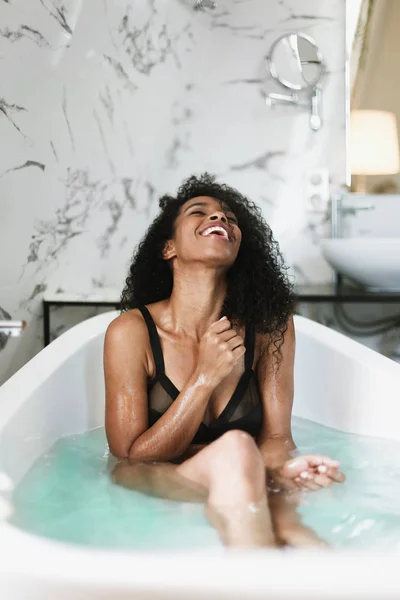 Młody ładny afro amerykański dziewczyna siedzący w kąpiel, ubrany czarny strój kąpielowy. — Zdjęcie stockowe