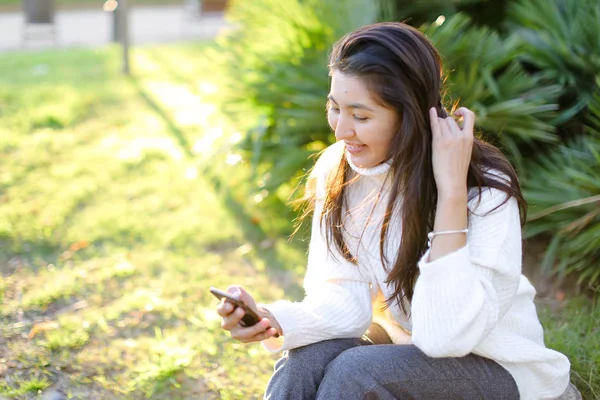 Chica japonesa sentada en el parque y utilizando el teléfono inteligente . — Foto de Stock