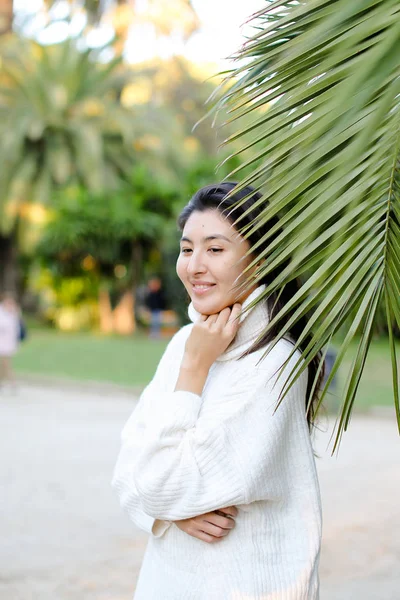 Menina bonita chinesa em suéter branco em pé perto da folha de palma . — Fotografia de Stock