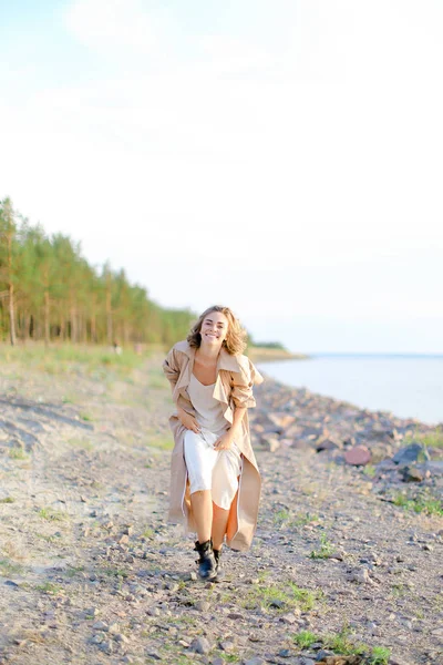 Uśmiechnięta młoda kobieta stoi na plaży morskiej z drzew w tle. — Zdjęcie stockowe