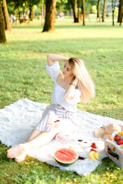 Parkta meyveli ekose üzerinde oturan genç sarışın kadın.. — Stok fotoğraf