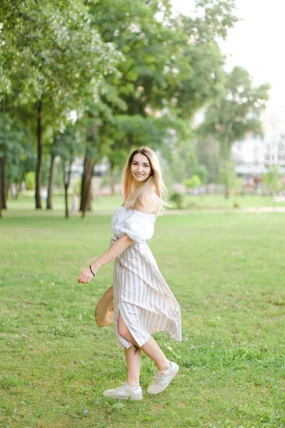 Giovane donna caucasica in piedi nel parco e mantenere il cappello . — Foto Stock