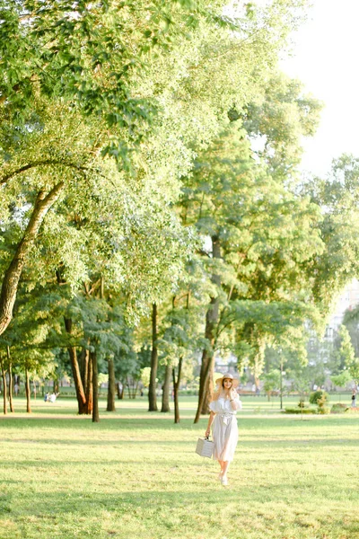 Giovane donna che indossa cappello passeggiando nel parco con borsa nella giornata di sole . — Foto Stock