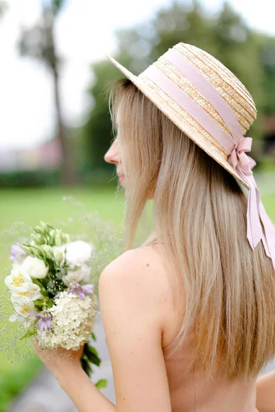 Rückansicht einer jungen blonden Frau in körperfarbenen Overalls und Hut mit Blumen. — Stockfoto