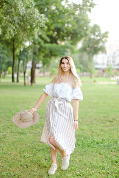 Junge Frau steht im Park und hält Hut. — Stockfoto