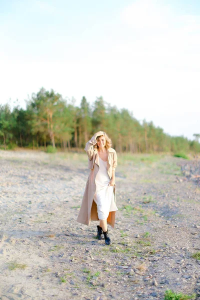 Fiatal európai nő sétál zsindely tengerparton, és visel nyári kabát. — Stock Fotó