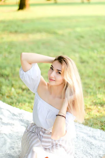 Ritratto di giovane ragazza bionda seduta su plaid, erba sullo sfondo . — Foto Stock