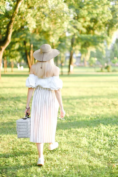 Back view of young caucasian woman in hat walking in park and keeping bag. — Stock Photo, Image