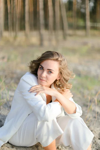 Jovem mulher sentada na praia de areia e vestindo roupas brancas . — Fotografia de Stock