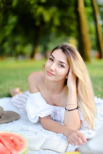 Young happy girl lying on plaid in park and reading book. — Stock Photo, Image