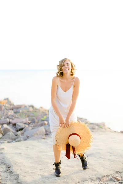 Giovane donna bionda che cammina sulla spiaggia rocciosa con hant in mano e indossa vestito . — Foto Stock