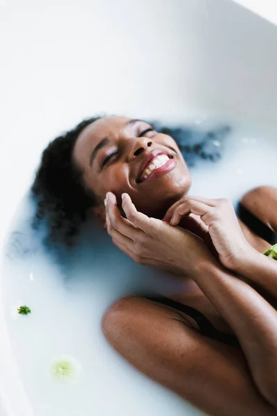 Mladá šťastná afro americká dívka se koupe a leží v pěně, na sobě plavky. — Stock fotografie