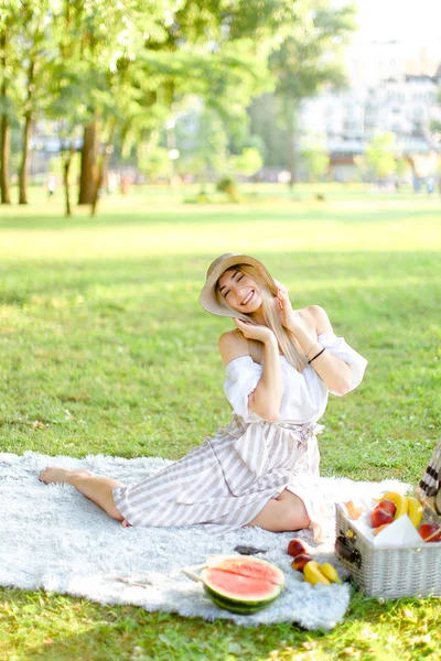 Jovem bela mulher sentada no parque em xadrez perto de frutas, grama no fundo . — Fotografia de Stock