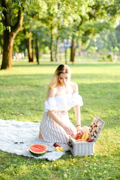 Ung flicka förbereder för picknick i parken, sitter på rutig nära låda och vattencitron. — Stockfoto