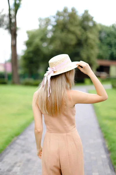 Back view of young blonde female person in body color overalls and hat. — Stock Photo, Image