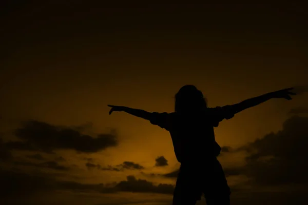 Silueta femenina oscura con las manos levantadas en el cielo marrón atardecer con nubes en Bali . — Foto de Stock